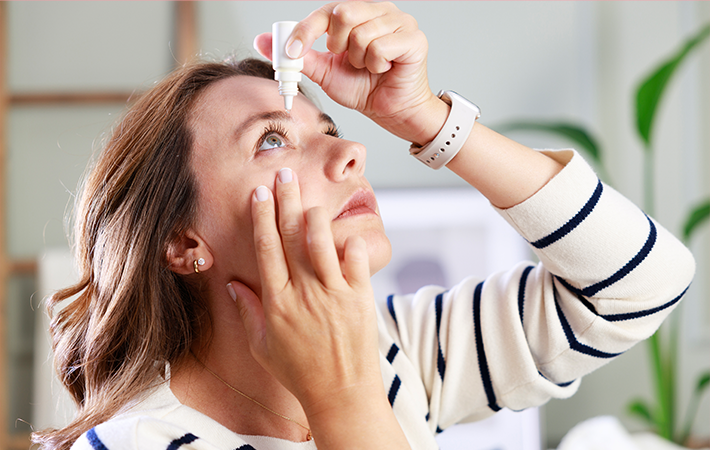 White woman looking up at the ceiling while pulling her bottom eye down to put on eye drops. 