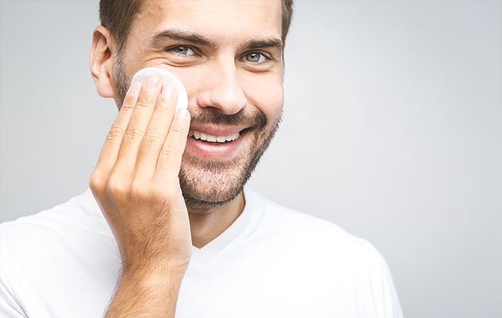 Image of white man in white shirt, smiling a the camera and holding a circular cleaning pad up to his right check.