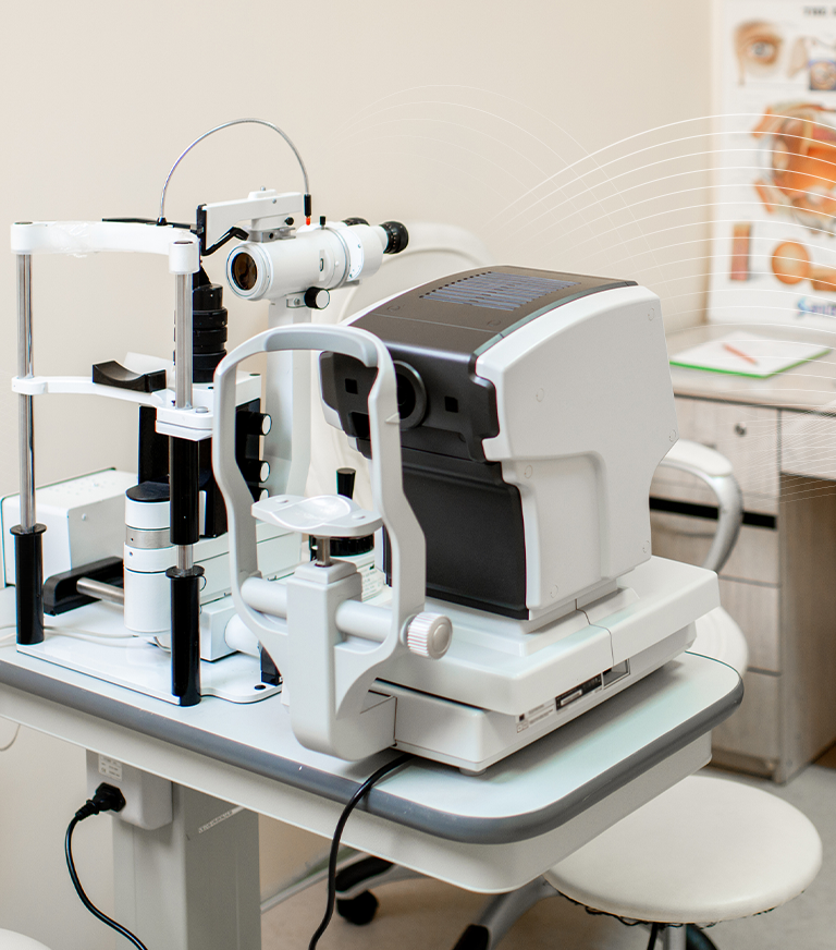 Mobile Hero Image: Wide shot of an Optometrist's office with eye examines equipment. There is a anatomical diagram of an eye on the back wall.